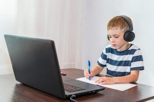 Niño concentrado usando auriculares y trabajando en el ordenador mientras aprende a escribir