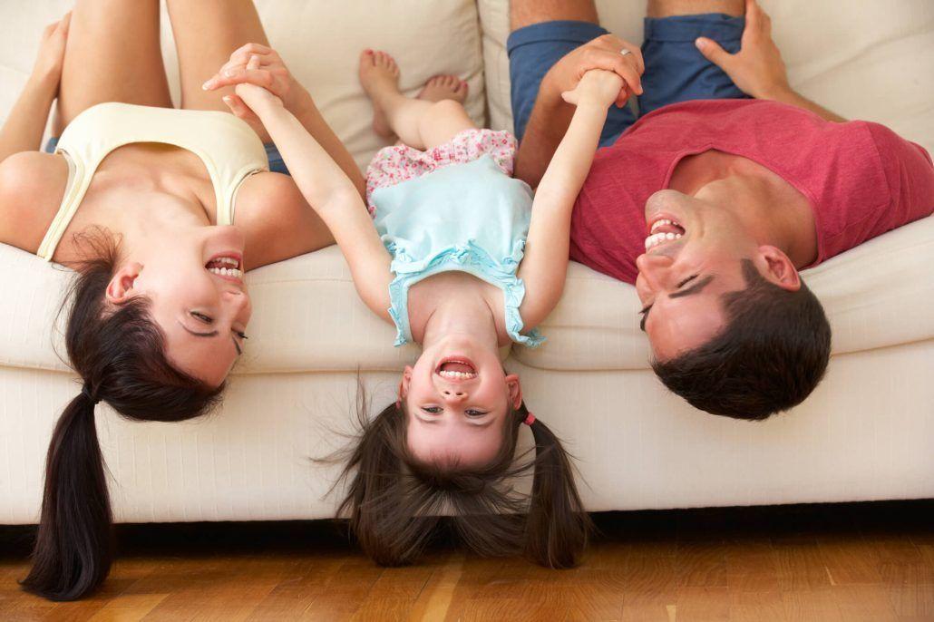 imagen de un padre y una madre jugando con su hija a a tumbarse a l revés en el sofá