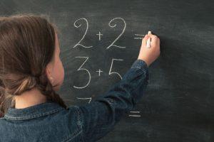 niña con discalculia haciendo sumas en la pizarra de la clase